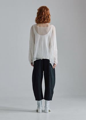 Person wearing a white blouse and dark pants standing against a plain background