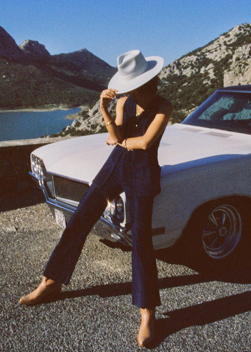 Person sitting on a classic car with mountains and water in the background