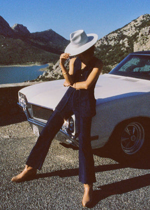 Person sitting on a classic car with mountains and water in the background