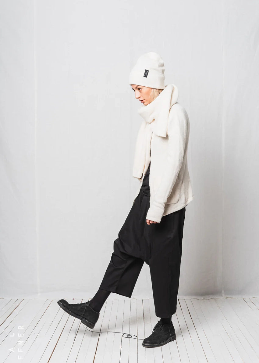 Person wearing a white beanie, scarf, and jacket with black pants against a white background