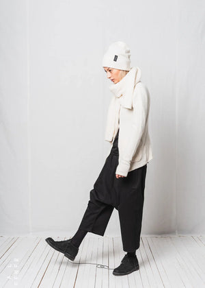 Person wearing a white beanie, scarf, and jacket with black pants against a white background