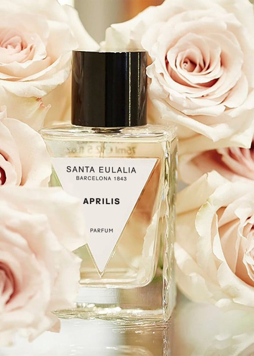 A bottle of 'Santa Eulalia Aprilis' perfume placed among pink roses, with the brand name and product name visible on the bottle.