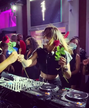 A person wearing a transparent reusable mask with a support for the chin and elastic bands, standing at a DJ booth.