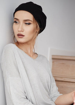A woman wearing a black cotton roll-up beanie hat from Kopka, with a flared top resembling a beret.