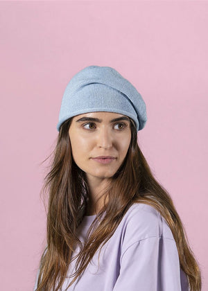 Woman wearing a grey beanie beret with a purple sweater on a pink background 