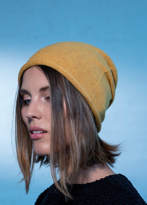 Woman wearing a yellow beanie beret with a black sweater on a blue background 