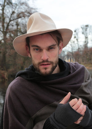 A person wearing a beige felt hat and a black jacket with a scarf tied around the neck.