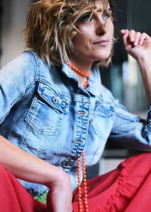 A person wearing a classic trucker jacket with a spread collar, front button closure, and chest button-flap pockets, seated with a pile of orange beads in their hand.