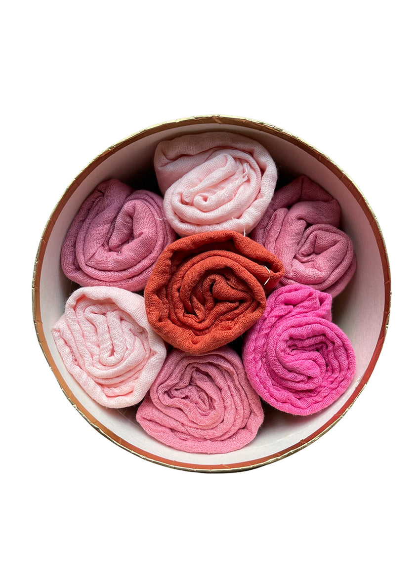 A collection of rolled-up scarves in shades of pink and red displayed inside a round basket.