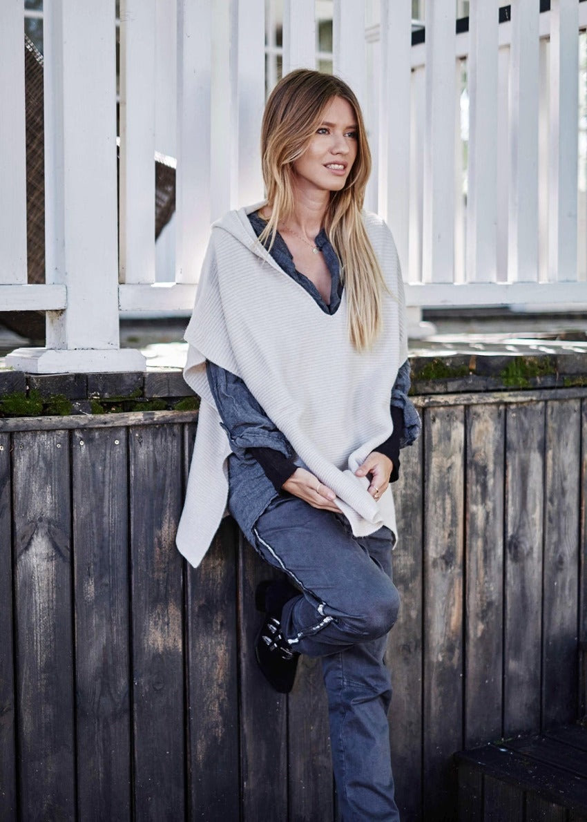 A person wearing a grey shirt with matching pants and a beige poncho