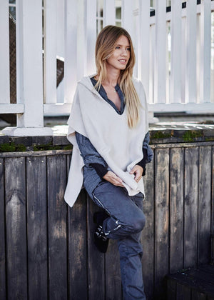 A person wearing a grey shirt with matching pants and a beige poncho