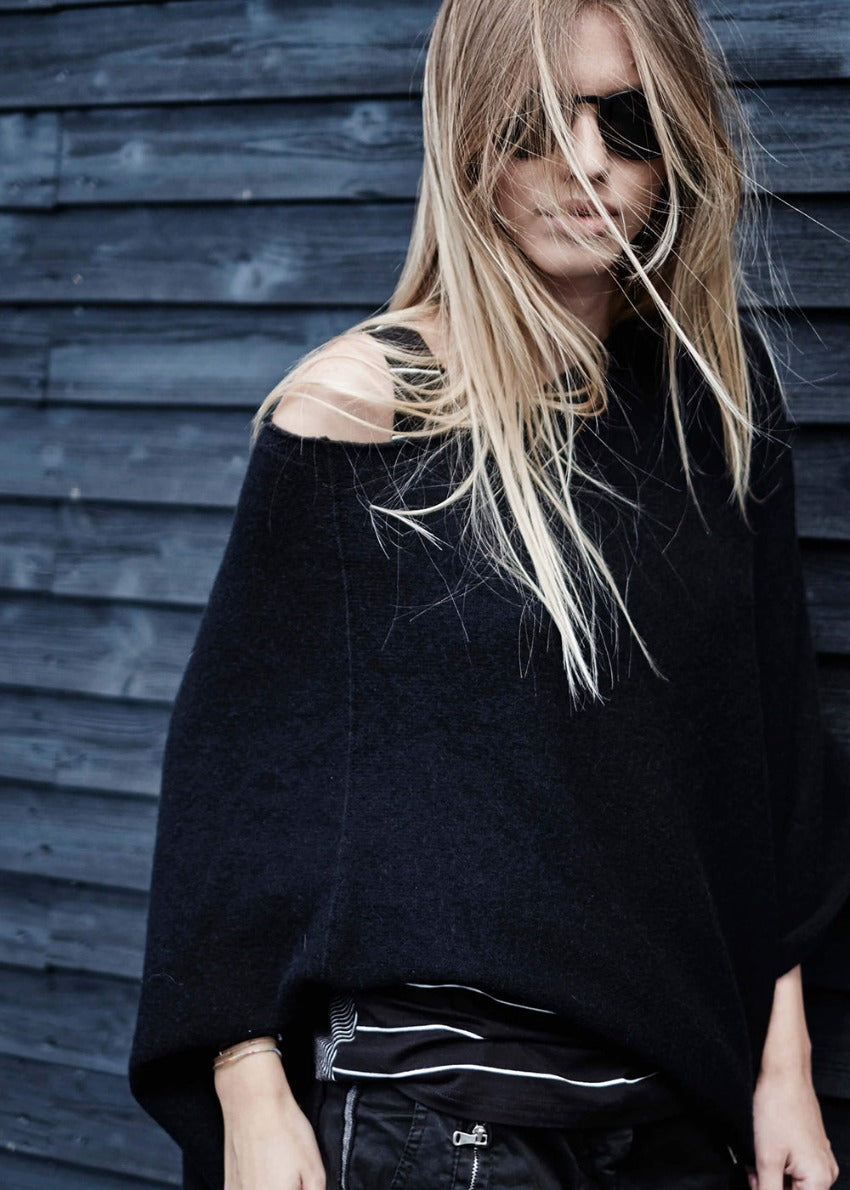 A person wearing a black poncho on a wood wall