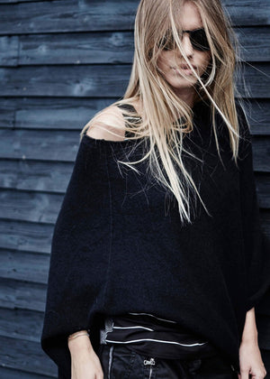 A person wearing a black poncho on a wood wall