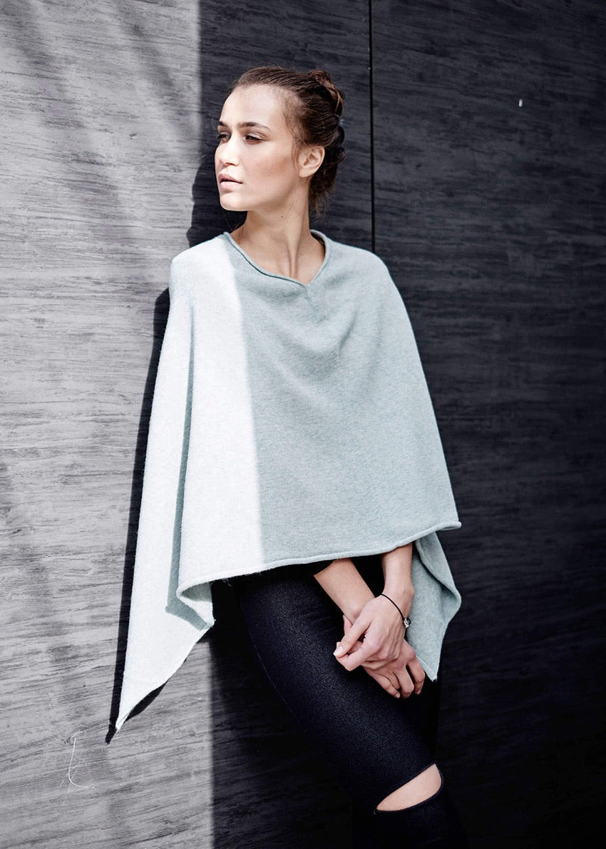 A person wearing a grey poncho on a wool wall