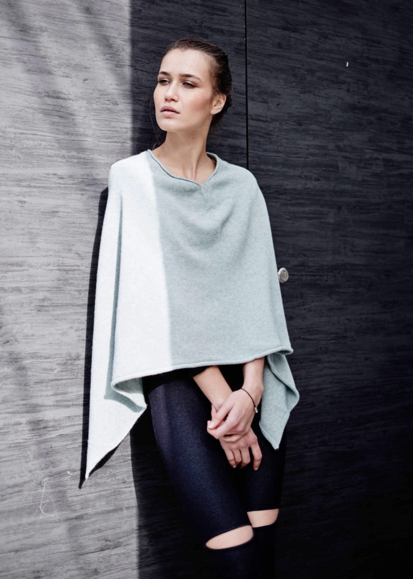 A person wearing a grey poncho on a wood wall
