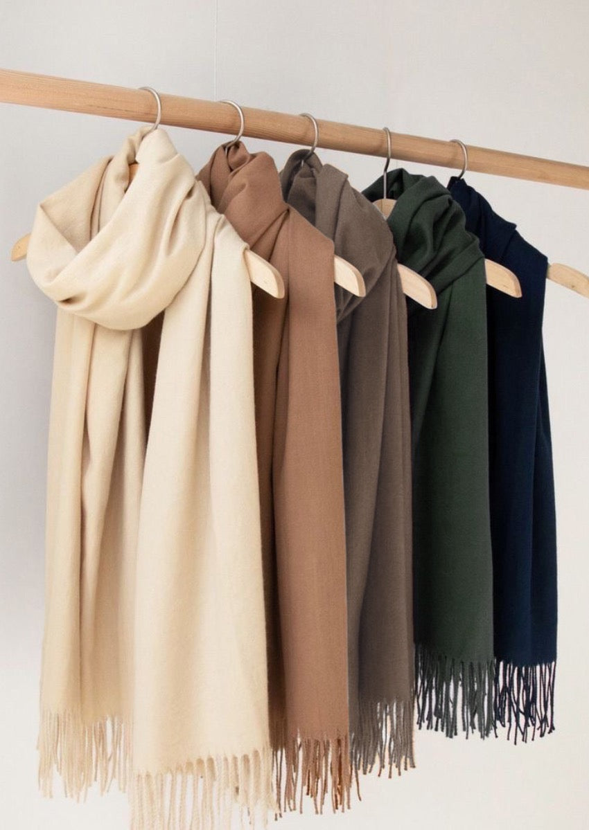 A collection of shawls in various colors hanging on wooden hangers, with a focus on a beige shawl at the bottom.