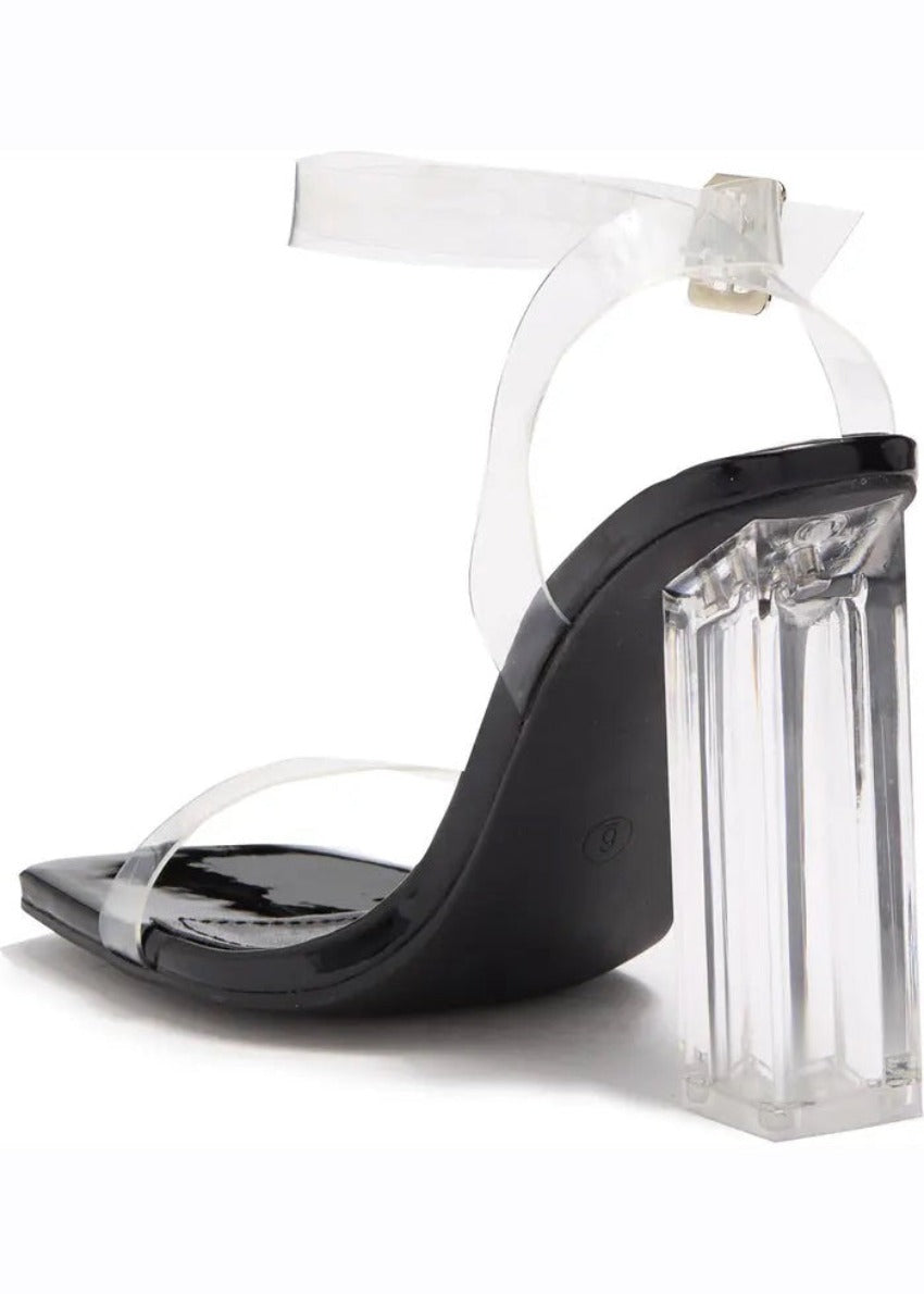A pair of clear lucite block heels with a chunky heel and a strap design