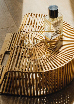 A bottle of Marinis - 75ml Floral Marine perfume placed on a wooden structure, with the sun casting shadows and highlighting the curves of the wood.