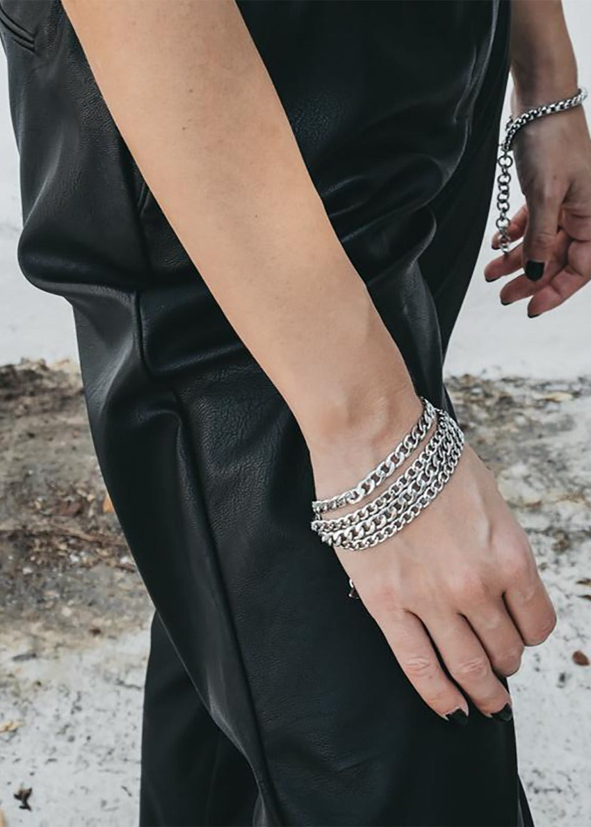 A person wearing a black leather jacket and a silver chunky chain bracelet.