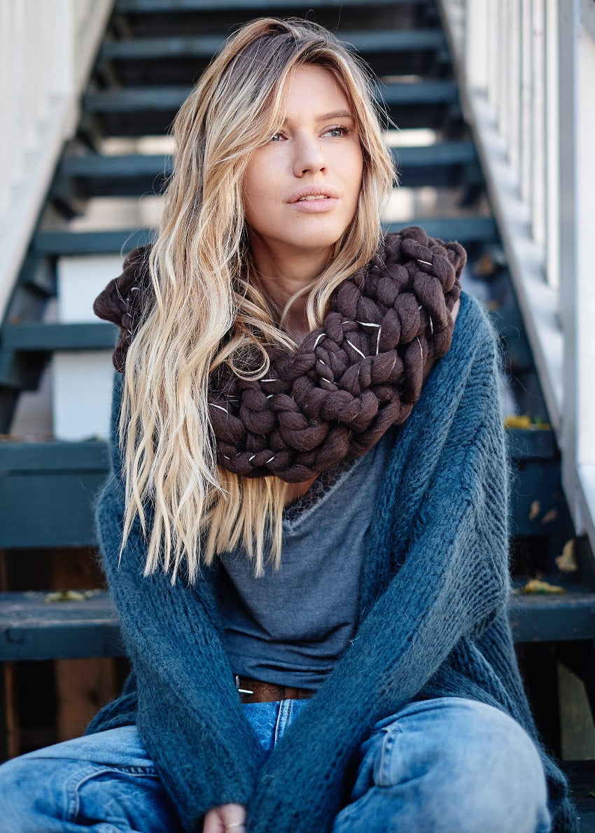 A person wearing a grey cardigan with jeans and a big brown scarf 