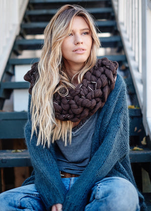 A person wearing a grey cardigan with jeans and a big brown scarf 