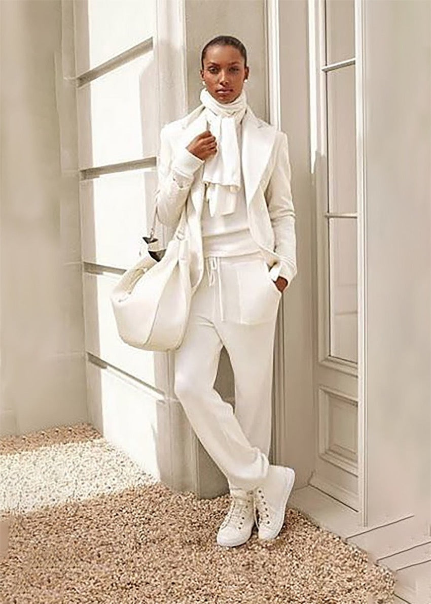 A person wearing a white knitted jogger pants with pockets and elasticized waist, paired with a white top and white shoes, standing indoors.