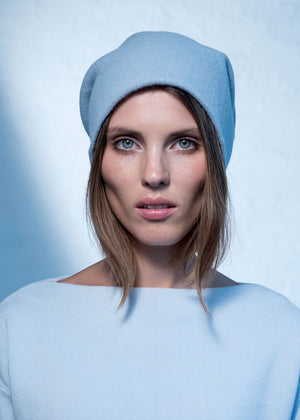 A person wearing a blue wool beanie with a white sweater