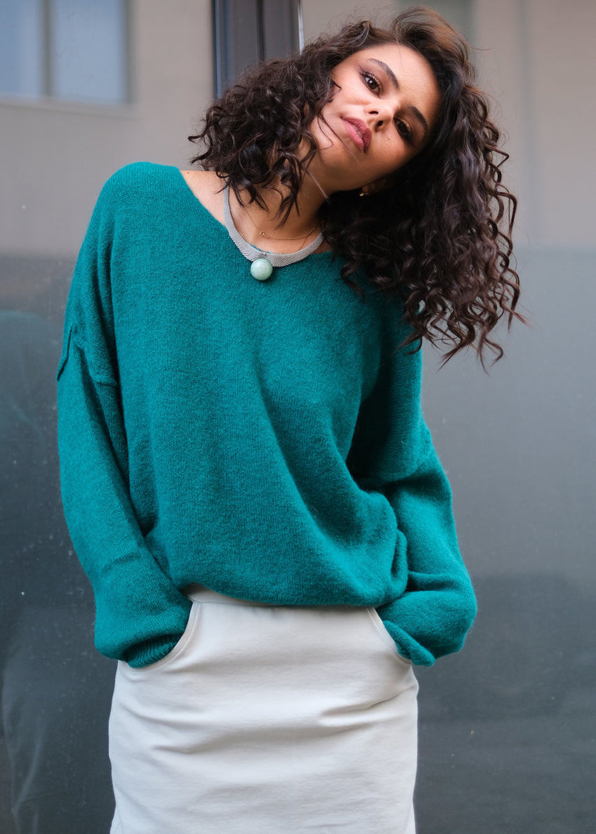 Person wearing a teal soft sweater with a white skirt with pockets