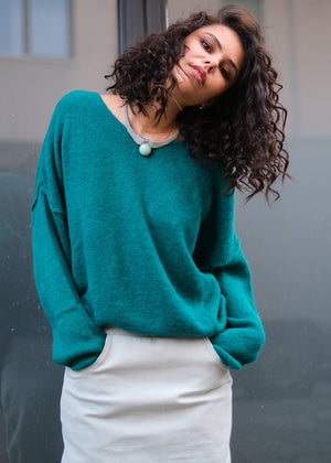 Person wearing a teal soft sweater with a white skirt with pockets