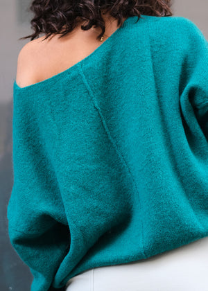 A person wearing a green, boxy fit cardigan with a deep V-neckline and long sleeves.