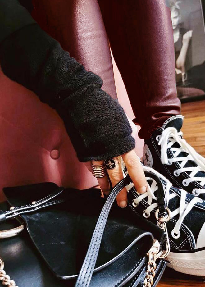 A close-up of a person wearing skinny-fit biker leggings in a brown-grey color, paired with a black top and sneakers, sitting next to a handbag.
