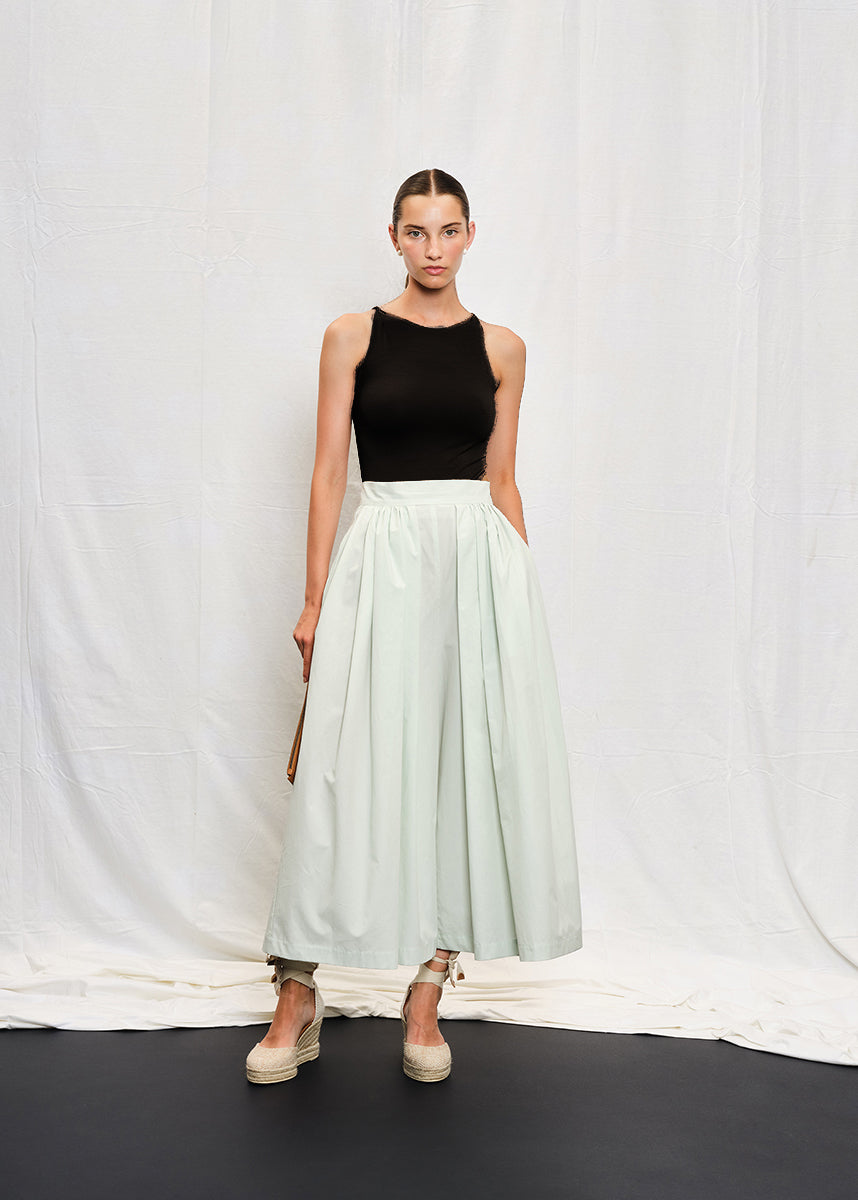 A person wearing a black sleeveless tank top with a V-shaped back and white skirt.