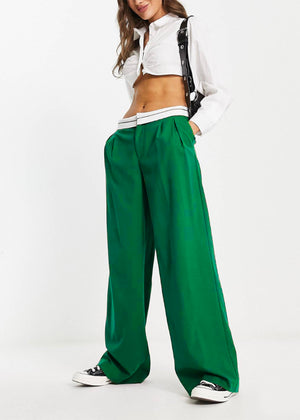 Person wearing a white crop shirt with green long wide pants on a white background 