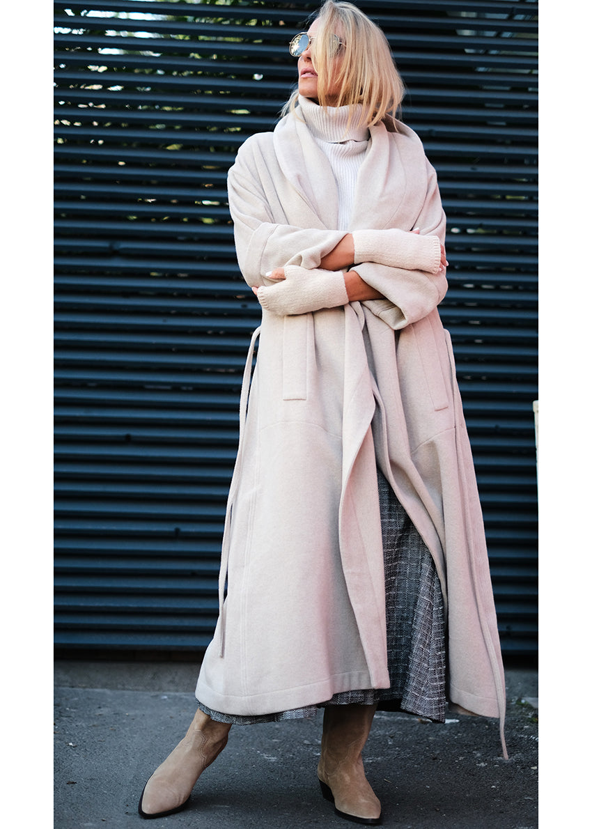 Woman wearing a beige wool coat hugging herself 