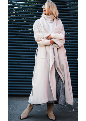 Woman wearing a beige wool coat hugging herself 
