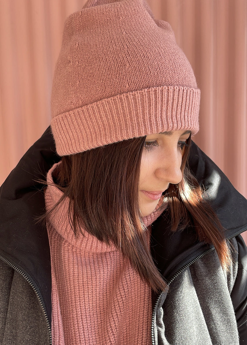 Person wearing a light pink warm beanie with matching sweater and a grey jacket