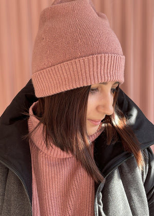 Person wearing a light pink warm beanie with matching sweater and a grey jacket