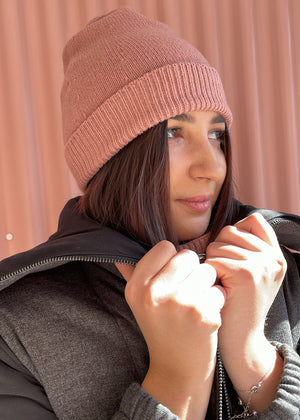 Person wearing a light pink warm beanie with a grey jacket on a pink background