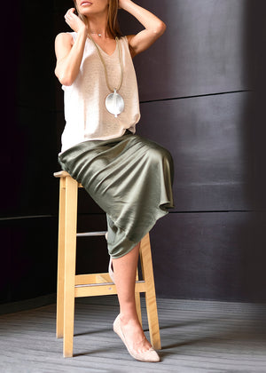 A person sitting on a chair wearing a beige tank top and a satin green khaki skirt 