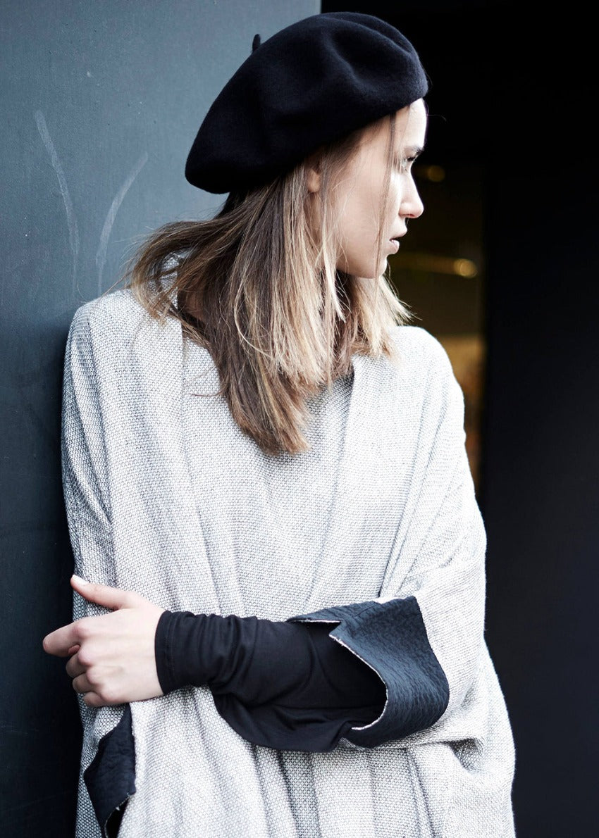 A woman wearing a black woollen beret and a grey, long-sleeved top with a high neck.