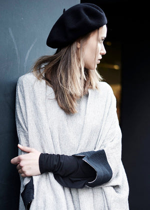 A woman wearing a black woollen beret and a grey, long-sleeved top with a high neck.