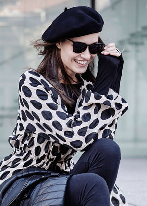 A person wearing a black wool beret with sunglasses and a dots jackets 