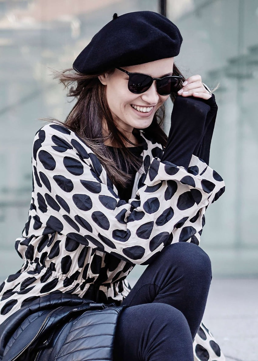 A person wearing a black wool conical beret with sunglasses and dots jackets